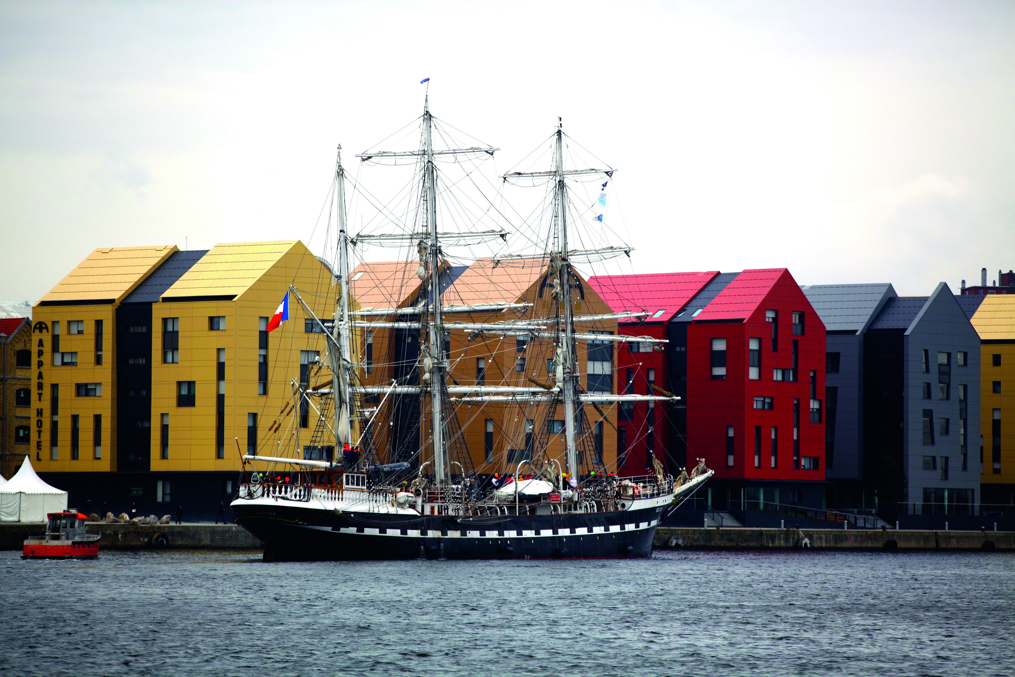 A tall ship docked in a harbor with colorful buildings in the background.