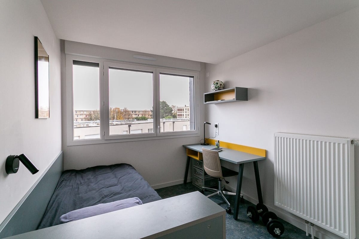 Une petite pièce, de taille modeste, comprenant un lit, un bureau et un radiateur.