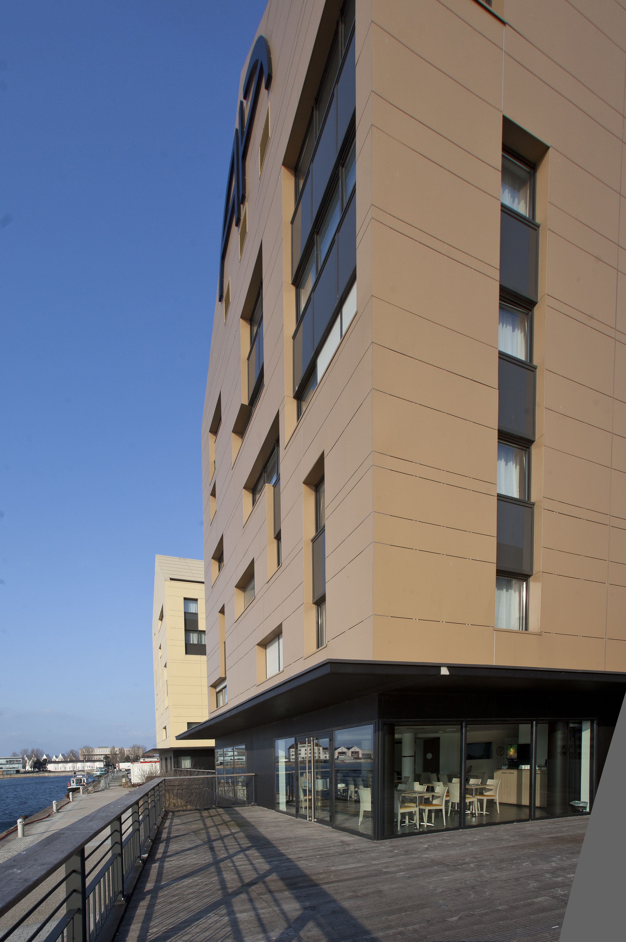 Un edificio moderno con techo plano, ventanas grandes y un área de balcón con mesas y sillas.