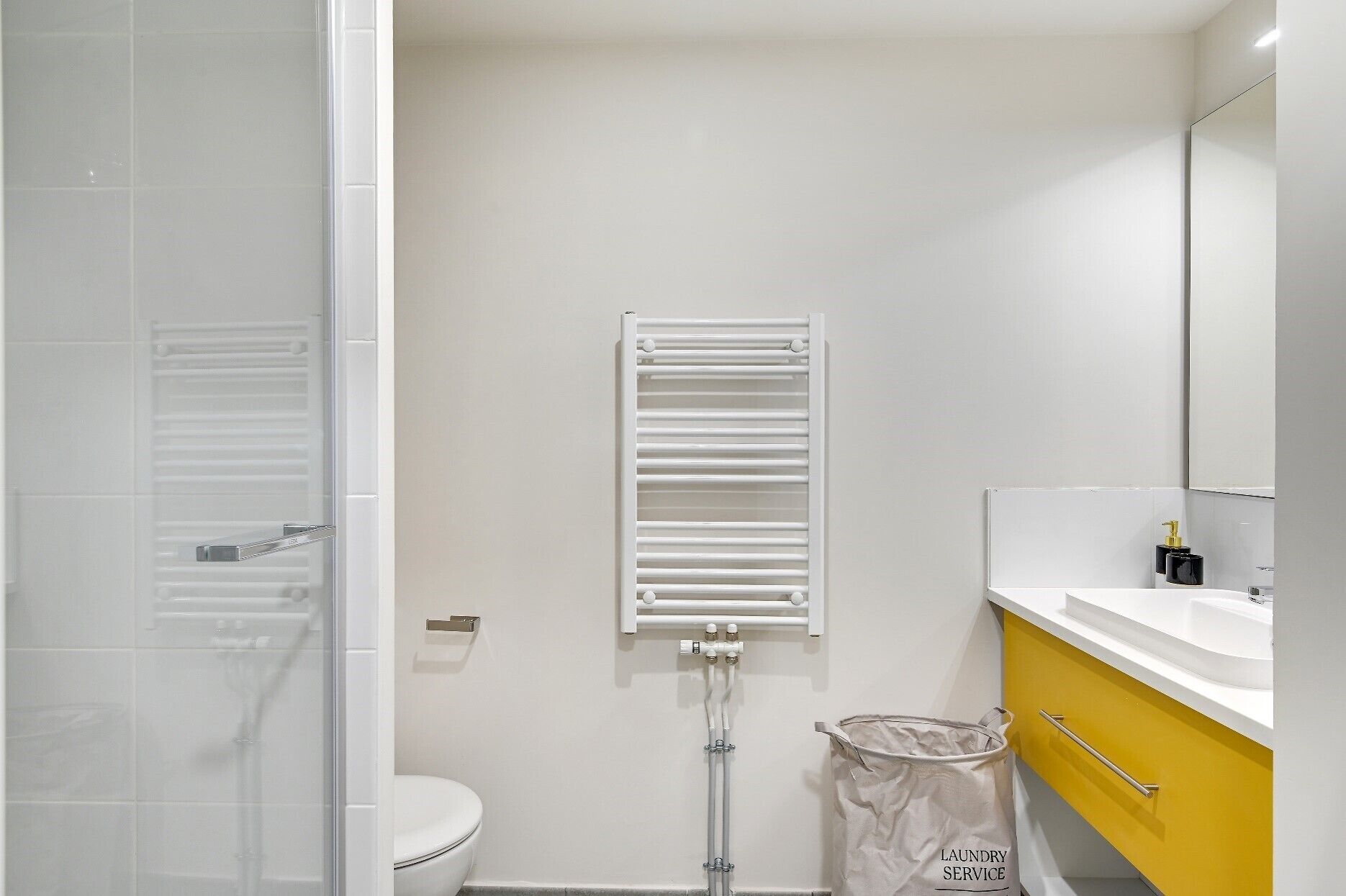 A bathroom with a white toilet, a towel rack, a mirror, and a yellow cabinet.