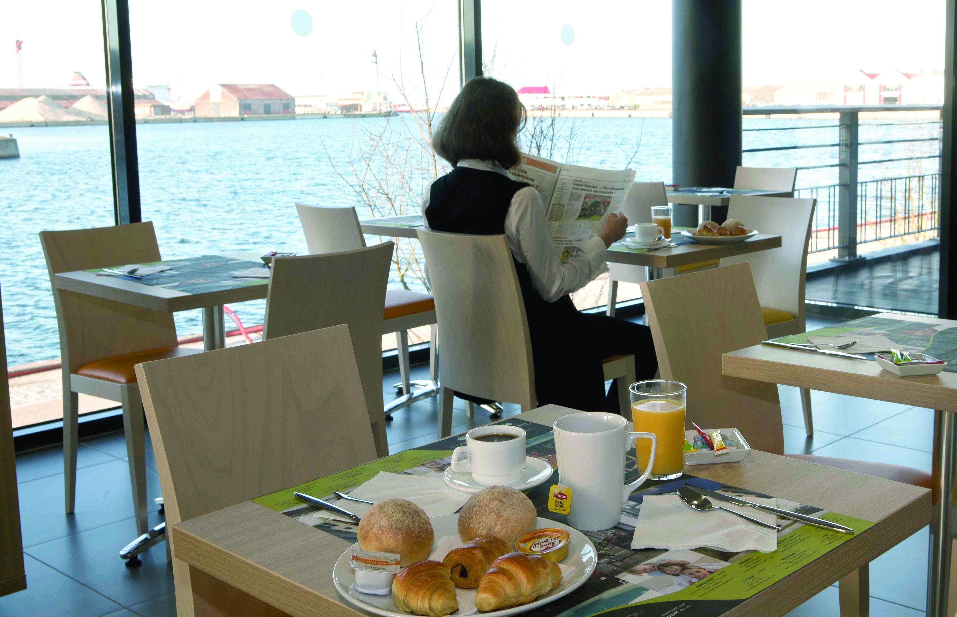 A dining area with a table set for breakfast, including croissants, coffee, and juice, overlooking a body of water.