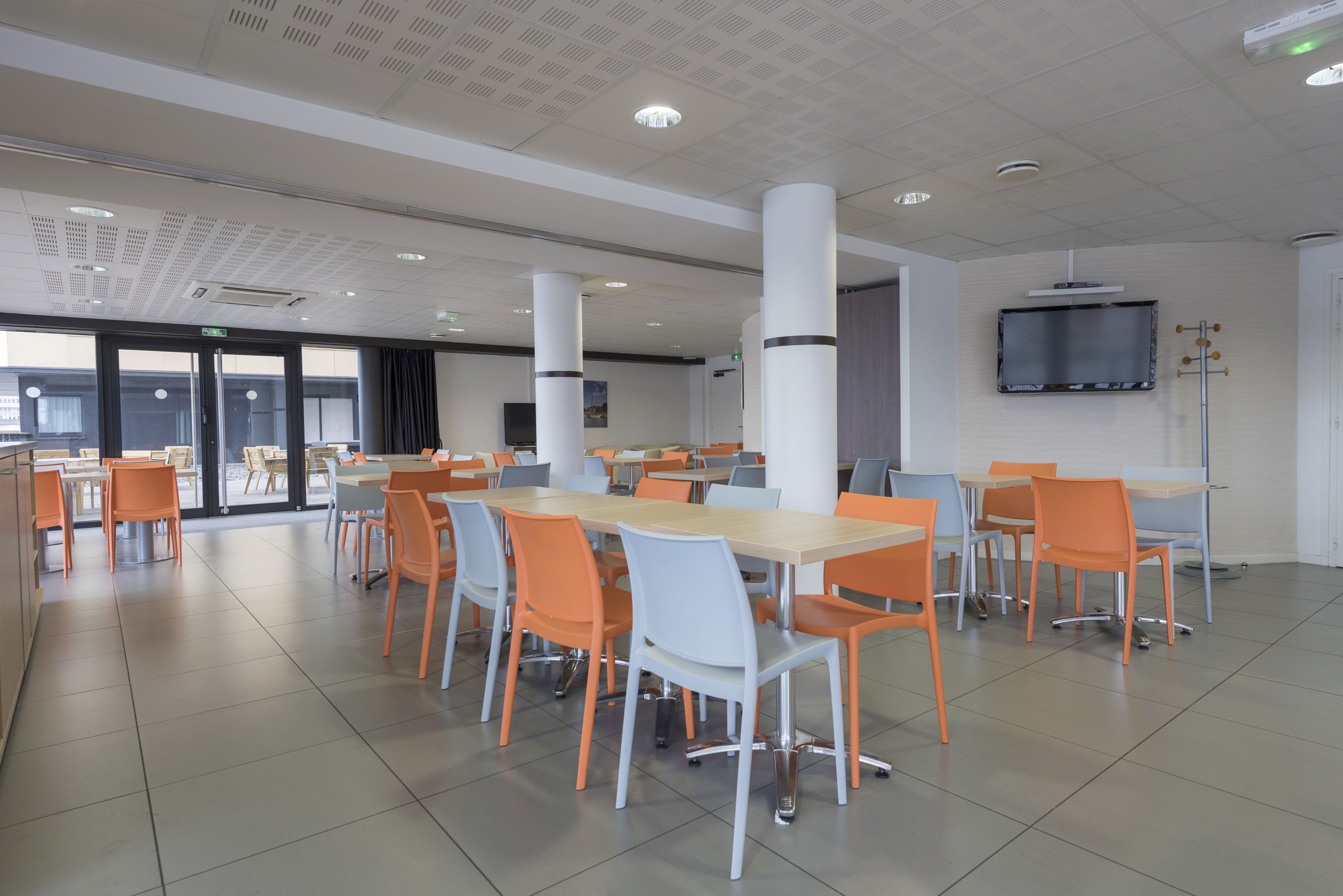 Una amplia cafetería con mesas y sillas altas, un televisor de pantalla plana montado en la pared y un ventanal que ofrece vistas al exterior.
