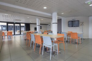 Una amplia cafetería con mesas y sillas altas, un televisor de pantalla plana montado en la pared y un ventanal que ofrece vistas al exterior.