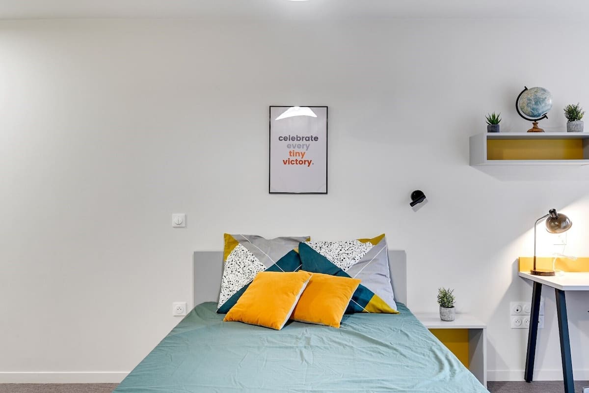 Une chambre à coucher bien rangée, avec un lit, une affiche motivante, un globe terrestre et une petite plante posée sur une étagère.