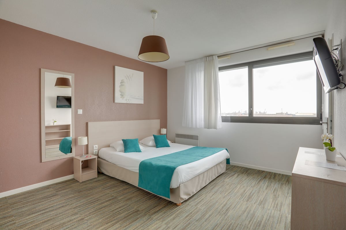Une chambre d’hôtel avec un lit, une table de chevet, une lampe et une fenêtre avec des rideaux.