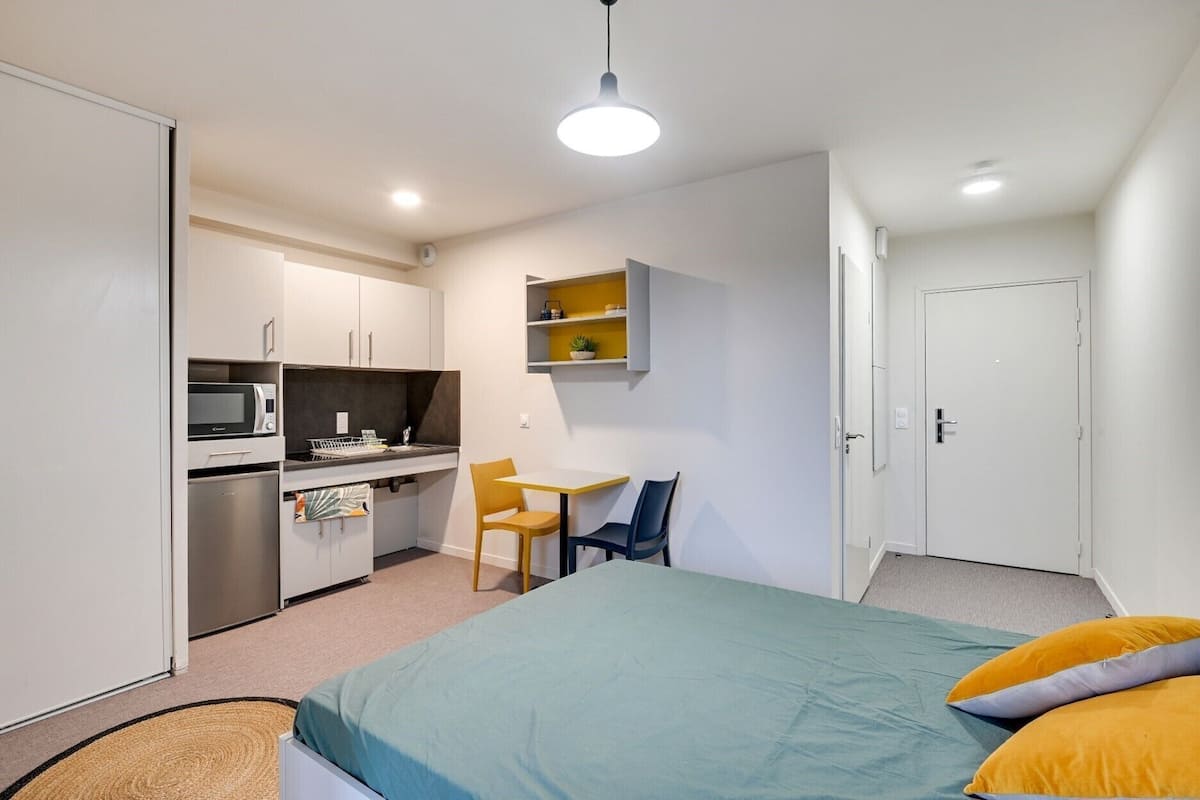 Une chambre compacte comprenant un lit, un bureau et une kitchenette.