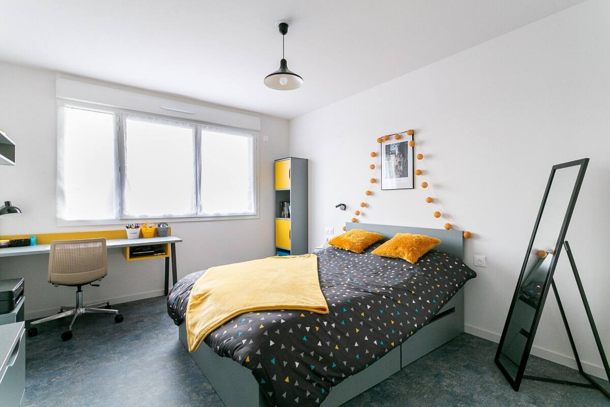Une chambre moderne avec un lit, un bureau, une chaise et un grand miroir.