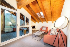 A modern living room with a sloped ceiling, large windows, a sofa, a coffee table, and a tripod with a ring light.