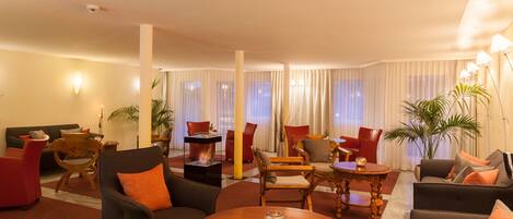 A spacious hotel lobby with multiple seating areas, including sofas and chairs, arranged around a central coffee table.