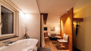A modern bathroom with a large bathtub, a small seating area, and a wooden accent wall. - Hotel Allalin Saas-Fee (Saas-Fee)