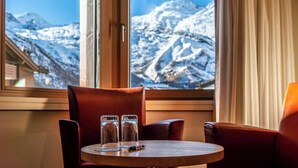 A cozy room with a wooden table and two leather chairs, a window with a view of snow-capped mountains. - Hotel Allalin Saas-Fee (Saas-Fee)