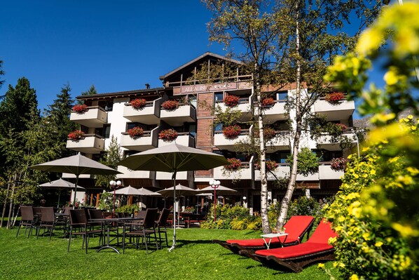 A hotel with outdoor seating, red lounge chairs, and a well-maintained garden.