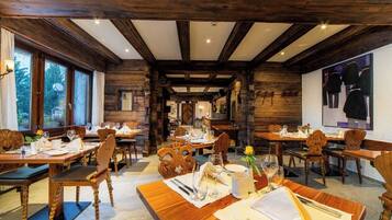 A rustic dining area with wooden beams, tables set for dining, and a view of the outdoors through large windows.