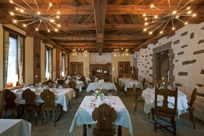 A dining area with multiple tables set for guests, wooden beams on the ceiling, and stone walls.