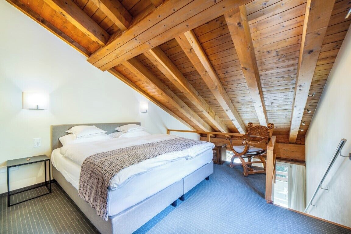 A bedroom with a sloped ceiling, a bed, a chair, and a small table.