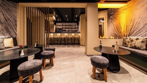 A modern bar area with a bar counter, stools, and a seating area with a sofa and round tables. - Hotel Allalin Saas-Fee (Saas-Fee)