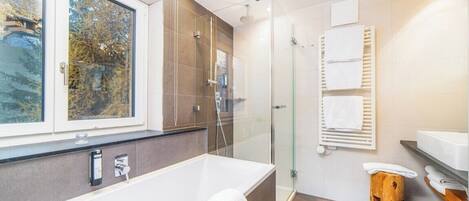 Un baño moderno con una bañera grande, cabina de ducha de vidrio y ventana con vistas a árboles.