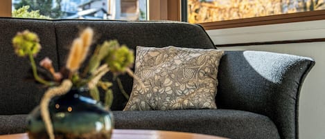 A dark gray sofa with a patterned cushion and a vase with dried flowers on a wooden table.