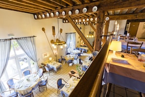 A dining area with multiple tables and chairs, wooden beams, and hanging light fixtures.