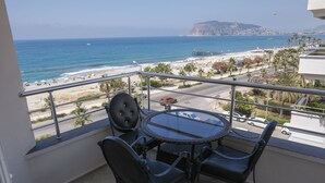A balcony with a round table and chairs, overlooking a beach and ocean. - Hotel Bella Bravo (Alanya)