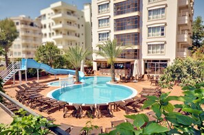 A pool area with lounge chairs, a blue slide, and a building with multiple balconies.