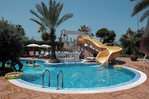 A swimming pool with a slide, lounge chairs, and palm trees.