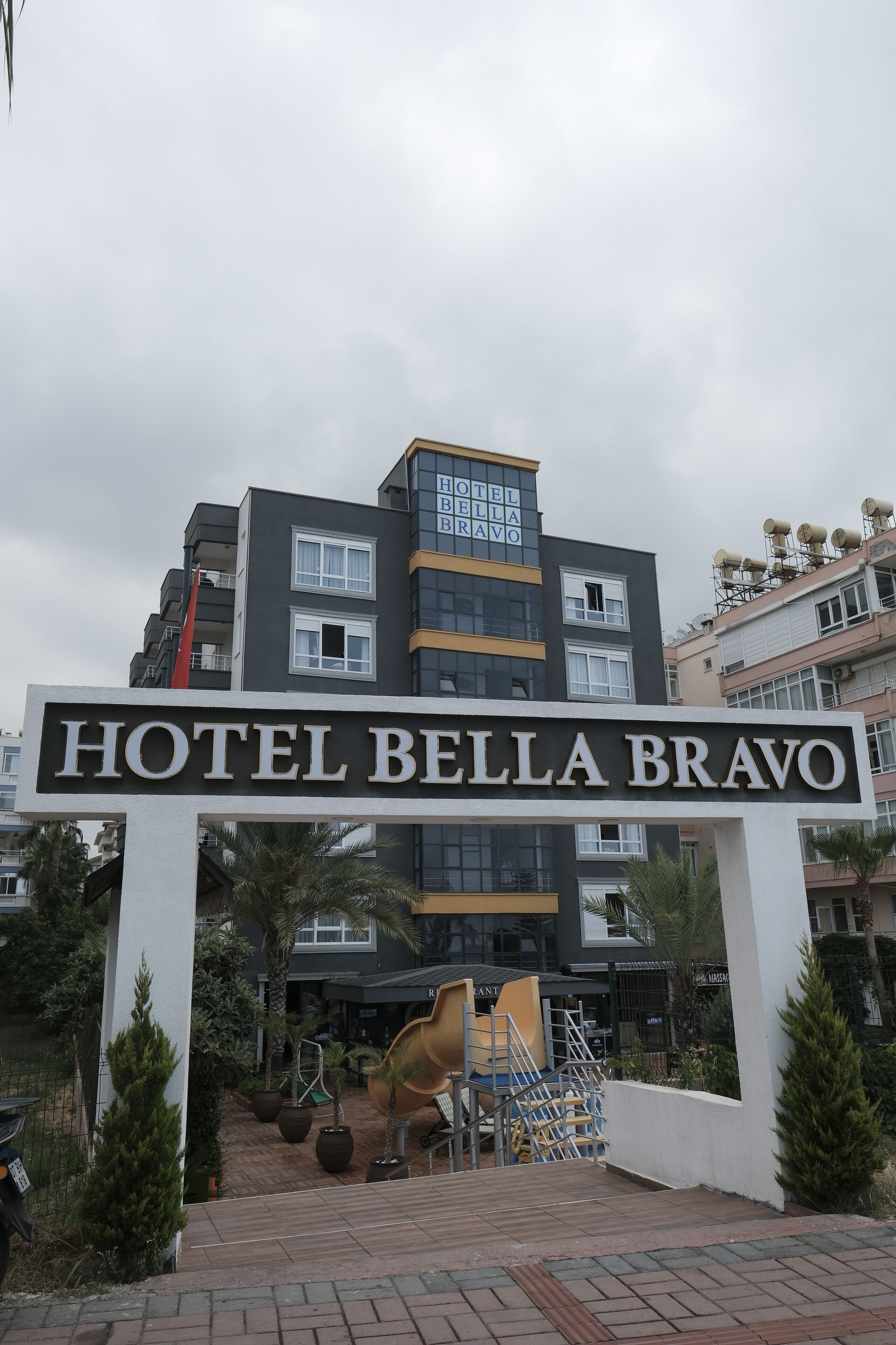 The entrance to Hotel Bella Bravo with a sign above the entrance, a staircase, and some potted plants.