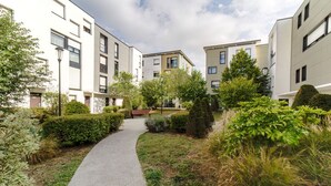 Un sentier traverse un quartier résidentiel, bordé d’immeubles d’appartements modernes, d’espaces verts bien entretenus et d’un banc.