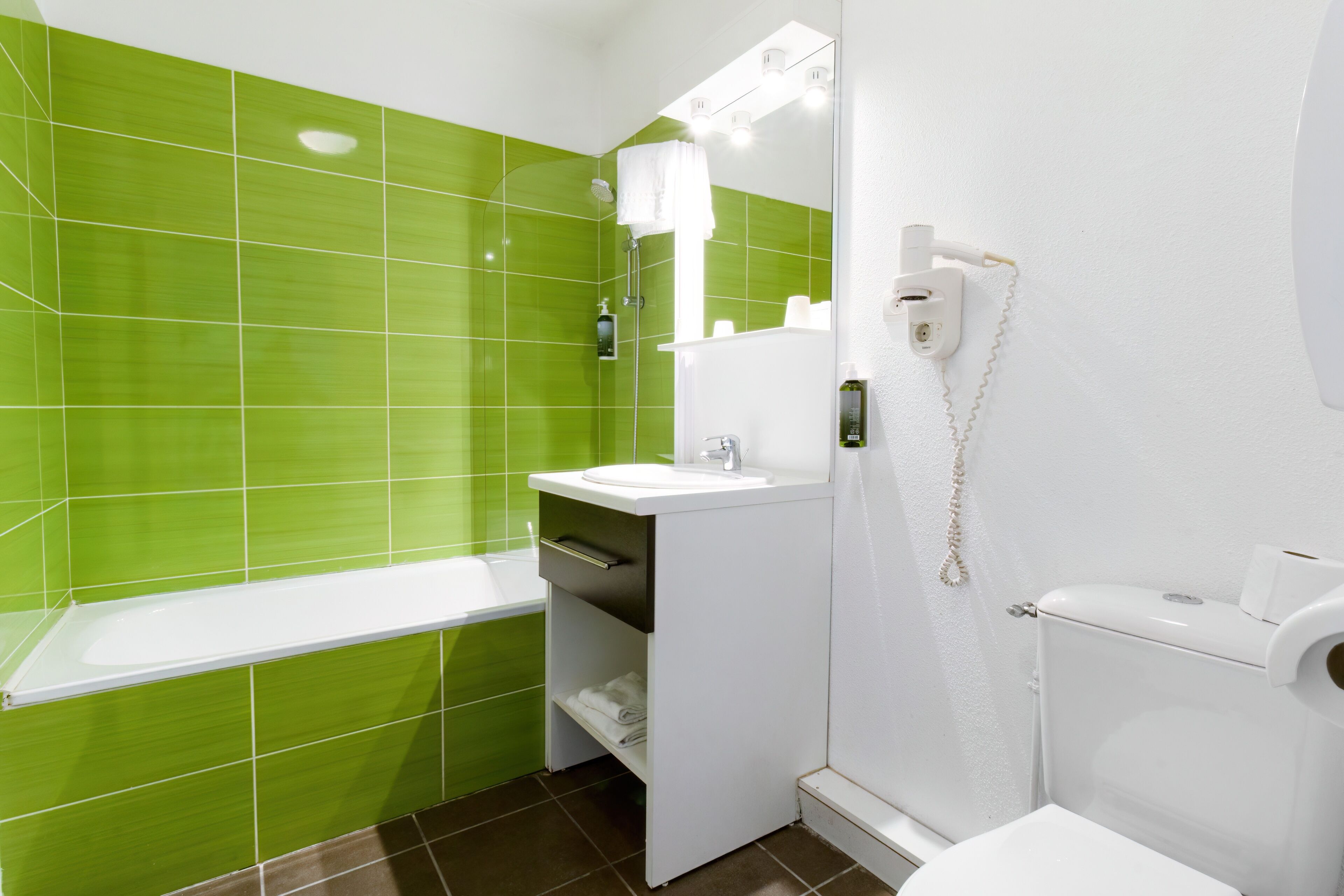 A bathroom with green tiles, a white sink, a mirror, and a toilet.