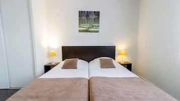 Ein Doppelbett mit zwei Kissen und einem Kopfteil, daneben zwei Nachttische mit Lampen, in einem Zimmer mit einem Bild an der Wand.