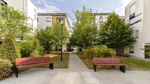 Une cour avec deux bancs en bois, un sentier et des bâtiments dotés de balcons.