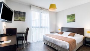 Une chambre d’hôtel équipée d’un lit, d’un bureau, d’une chaise, d’une télévision et décorée avec des œuvres d’art aux murs.