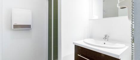 A modern bathroom with a white sink, dark wooden cabinet, and a glass shower enclosure.