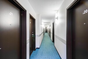 Corredor de hotel com portas numeradas 321 e 320, piso carpetado e luminárias fixadas na parede.