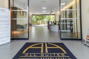 A hotel entrance with a reception desk, a waiting area, and a view of the outdoors.