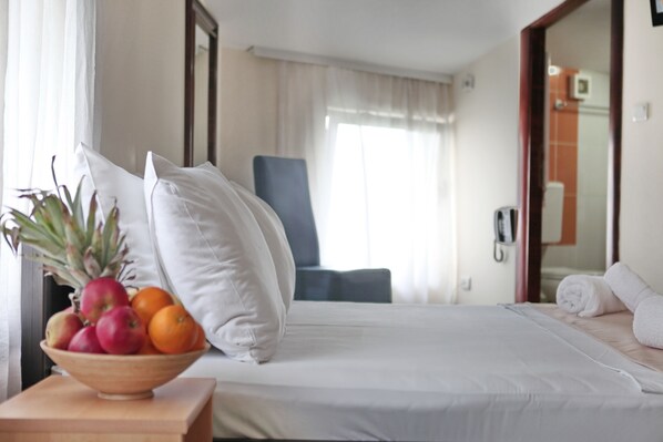 A hotel room with a bed, a bedside table with a fruit bowl, a chair, and a bathroom visible through an open door.