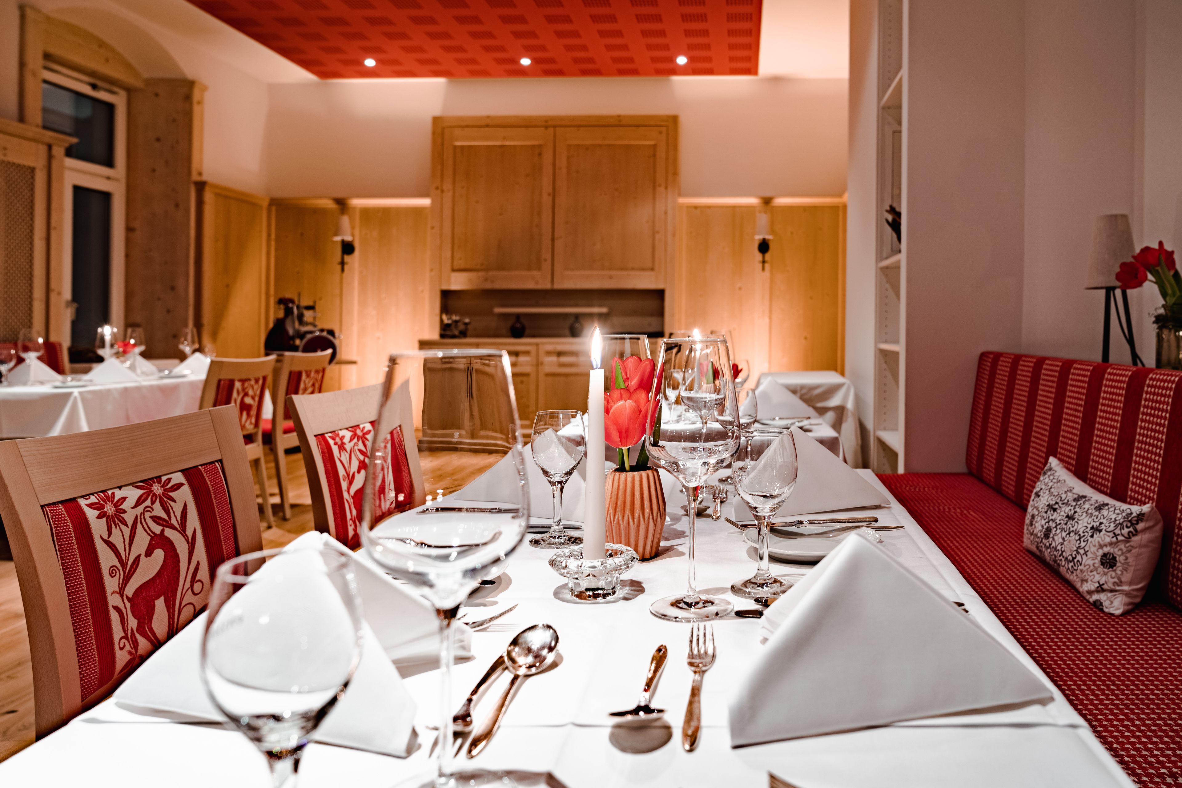 A dining area with a long table set for a meal, wooden cabinets in the background, and a red sofa with floral cushions.