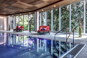 An indoor swimming pool with red chairs and large windows overlooking a forest. - Blatter's Hotel Arosa & Bella Vista SPA (Arosa)