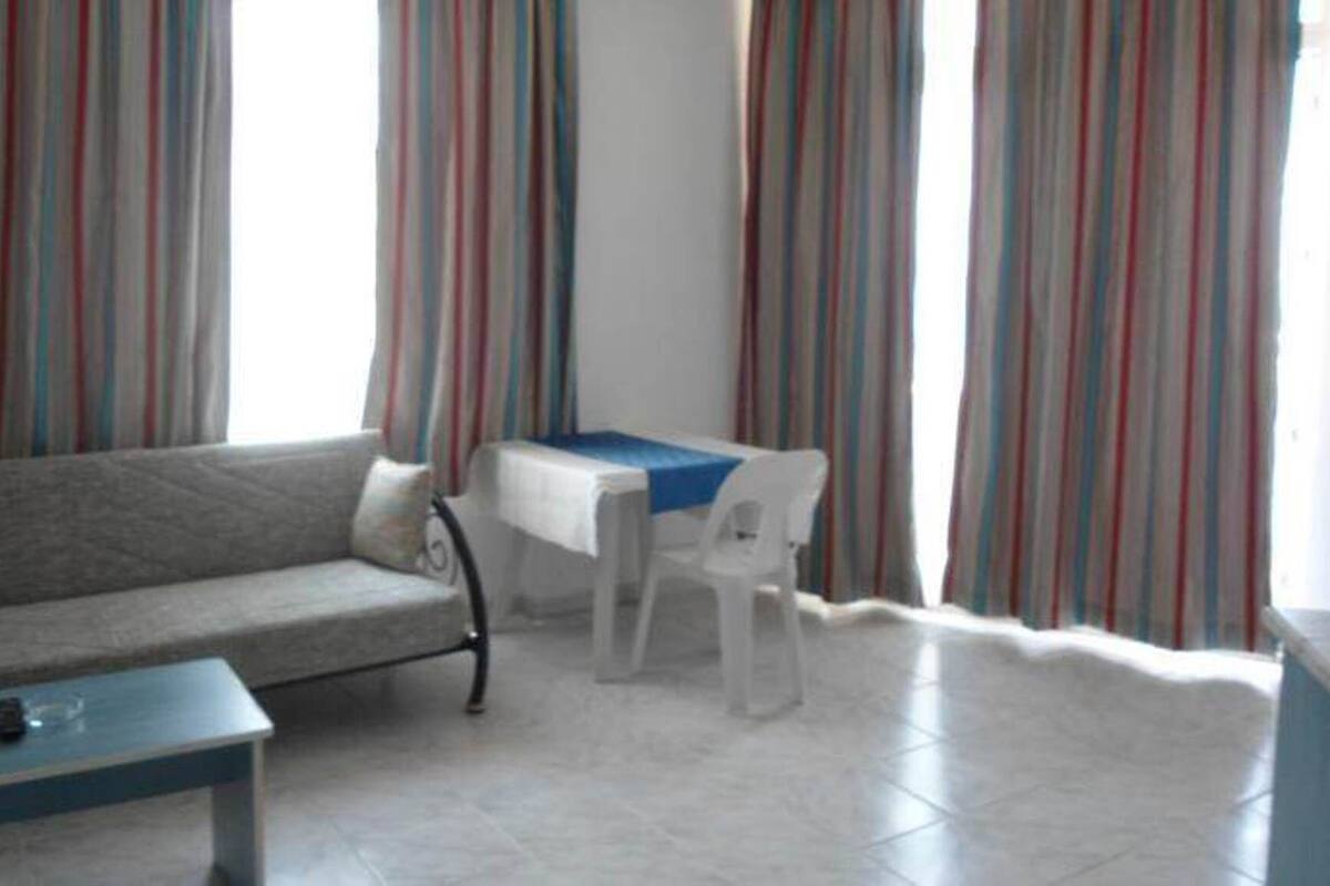 A living room with a sofa, a small table, a chair, and a table with a blue tablecloth.