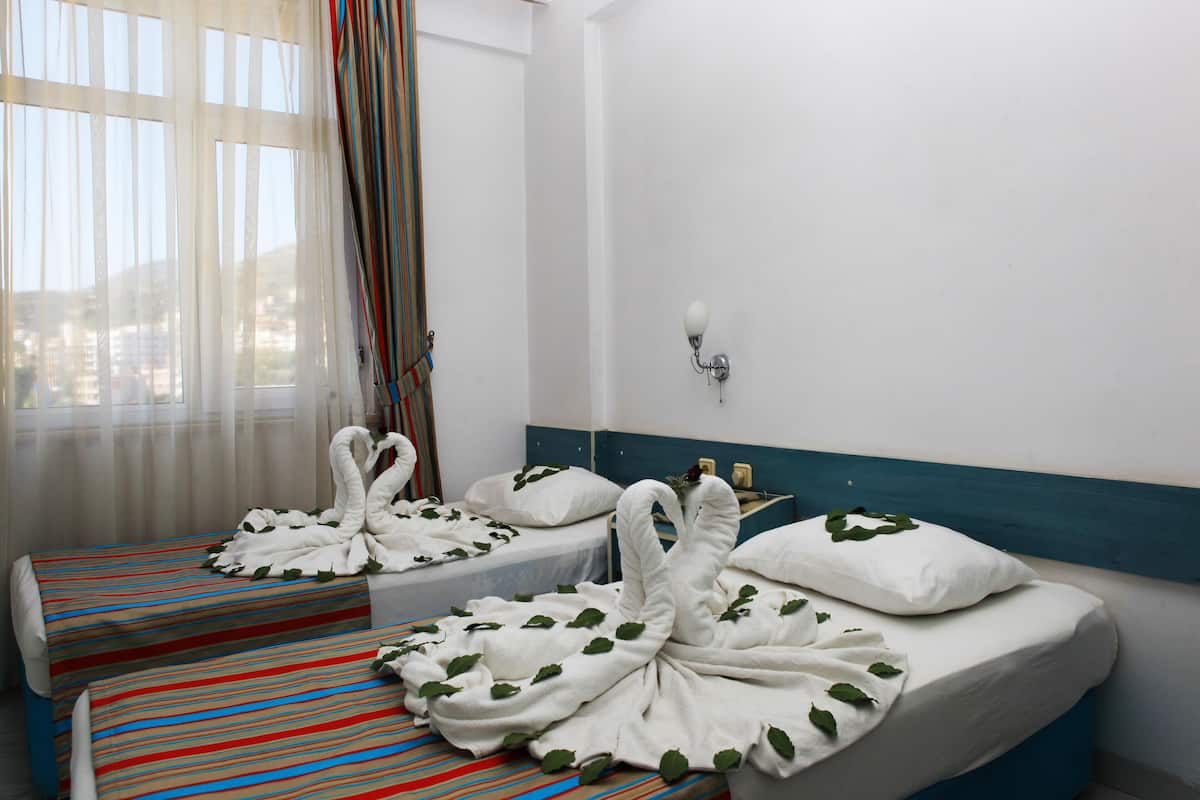 A hotel room with two beds, each adorned with white towels shaped like swans and green leaves.