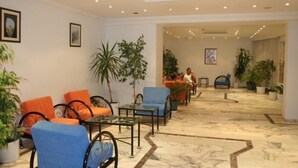 Un hall d’entrée avec des coins salon, des plantes en pot et des tableaux encadrés aux murs.