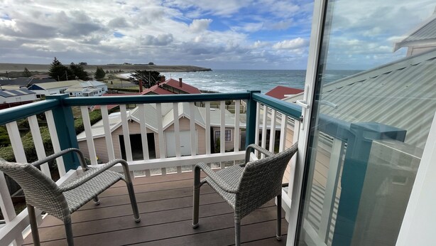 A balcony with wicker chairs, a view of the ocean, and a cloudy sky. - Hanlon Guest House (Stanley)
