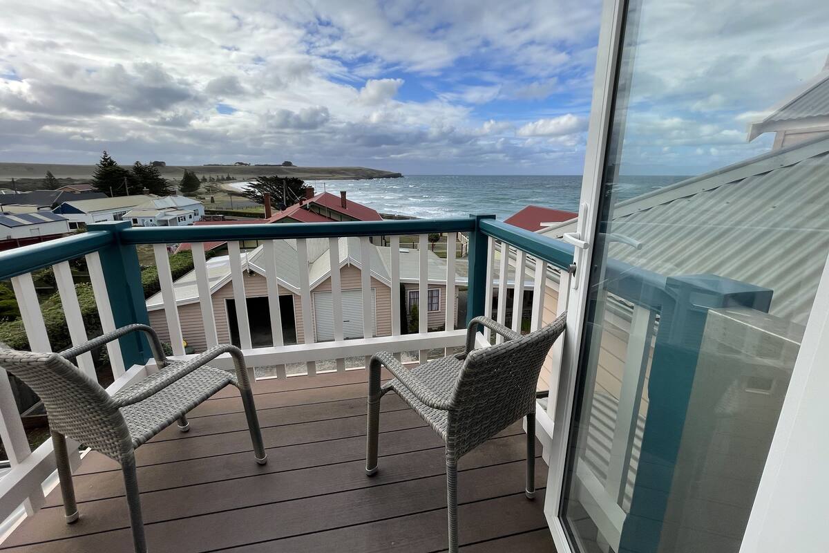 A balcony with wicker chairs, a view of the ocean, and a cloudy sky.