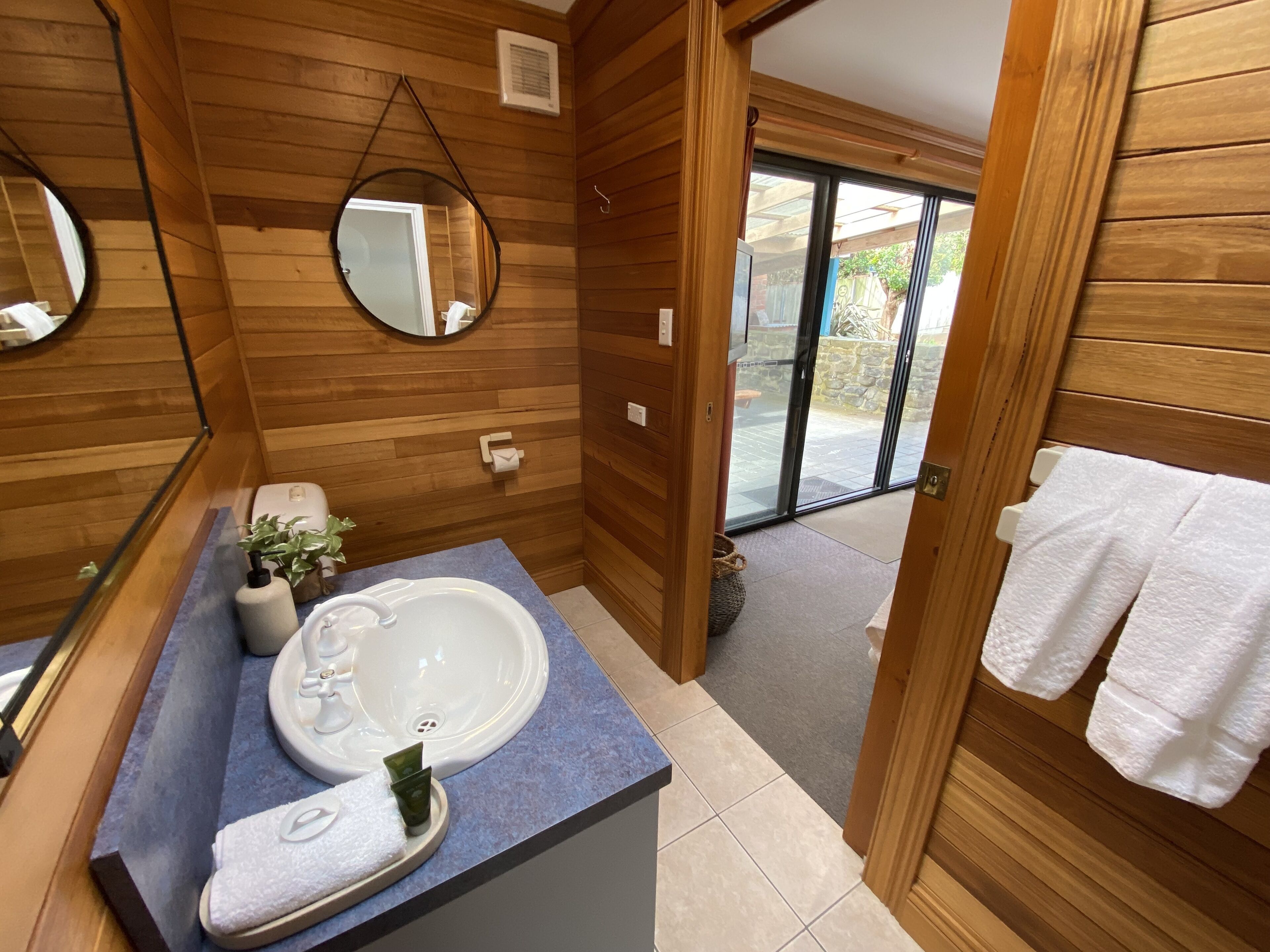 Une salle de bain aux murs lambrissés, équipée d’un lavabo, d’un miroir et de serviettes.