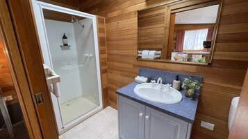 A bathroom with a glass-enclosed shower, a sink with a blue countertop, and wooden paneling on the walls.