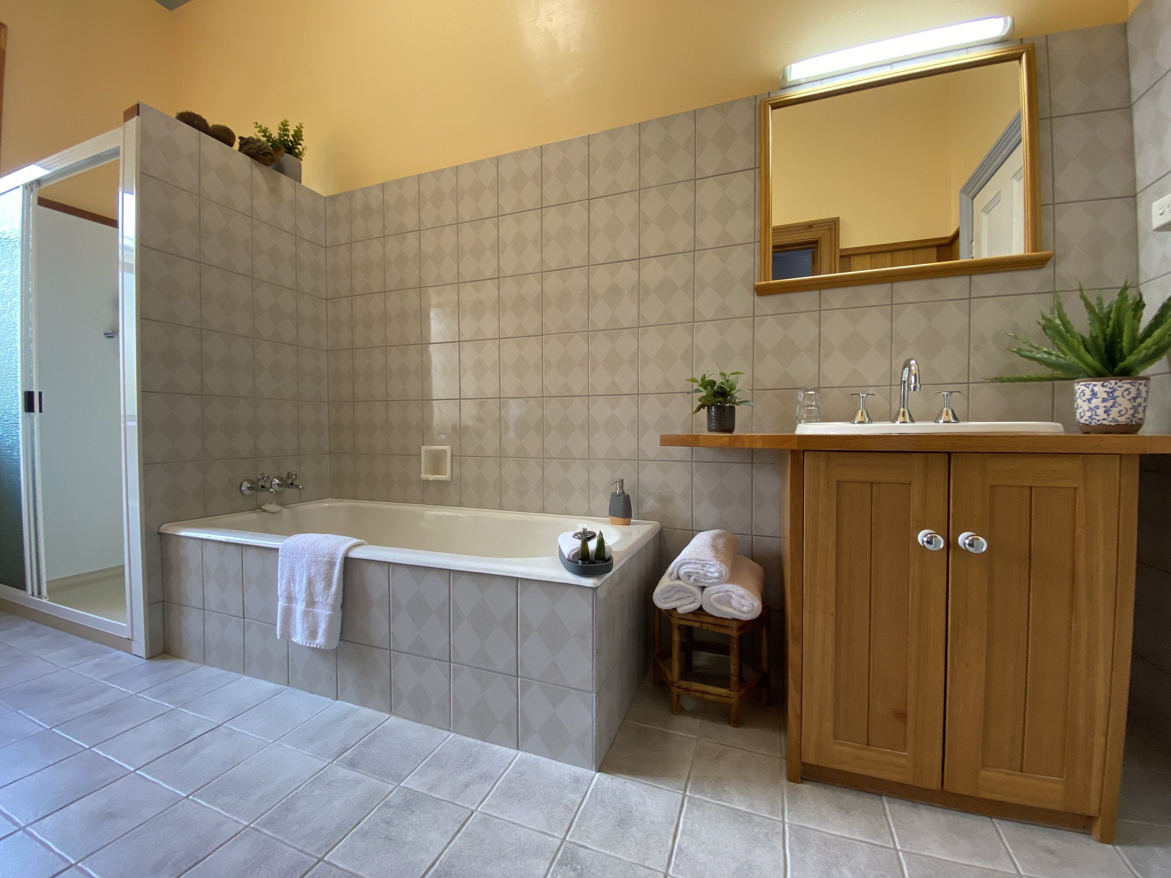 Une salle de bain avec une baignoire, un meuble-lavabo en bois avec un évier, un miroir et un petit tabouret.