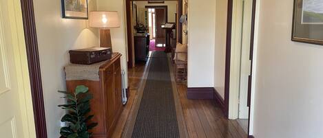 A hallway with wooden flooring, a radiator, a potted plant, a lamp, and a suitcase on a dresser.