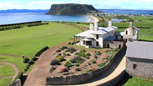 A historic stone building with a garden in front, overlooking a coastal area with a large body of water and a distant island. - Hanlon Guest House (Stanley)