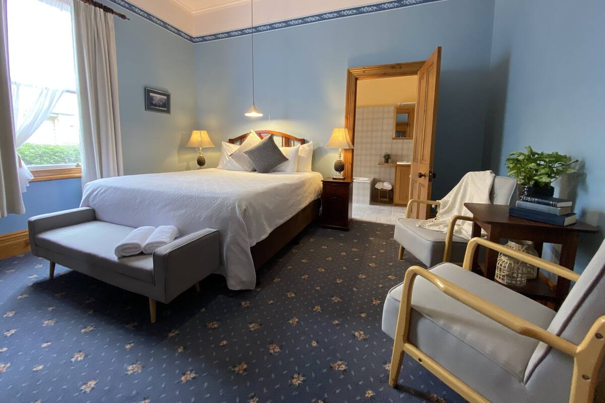 A hotel room with a bed, two bedside tables, a chair, a desk, a mirror, and a window with curtains.