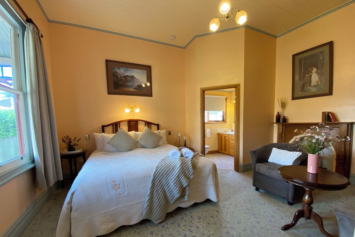 A hotel room with a large bed, a sitting area with a table, and a view of the outside.